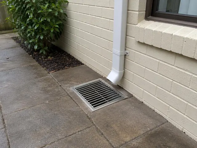 Outdoor gully grate beside a brick wall and paved path, clean and reinstated in Carlingford
