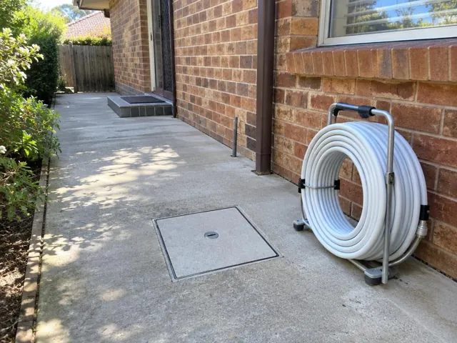 Concrete side path with a capped access cover beside a brick house and garden in Pennant Hills